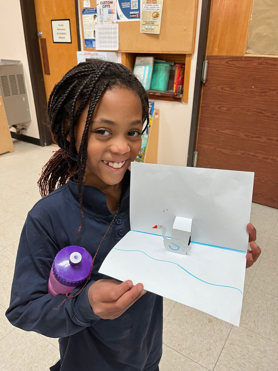 A smiling student holds up her pop-up science project